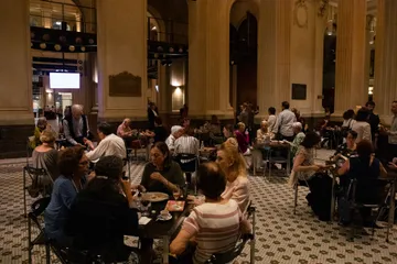 O Bar-café da Sala São Paulo é um espaço amplo, com mesas espalhadas. Pessoas estão sentadas em grupos, tomando café e comendo.