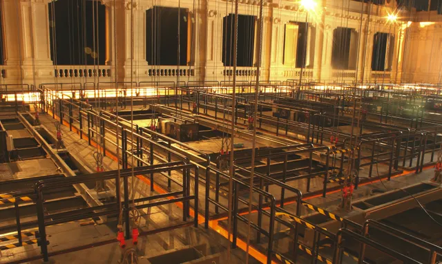 A imagem mostra o forro do teto da Sala São Paulo. É possível ver os cabos que sustentam as placas e o espaço de trabalho acoplado em cima de cada estrutura.  