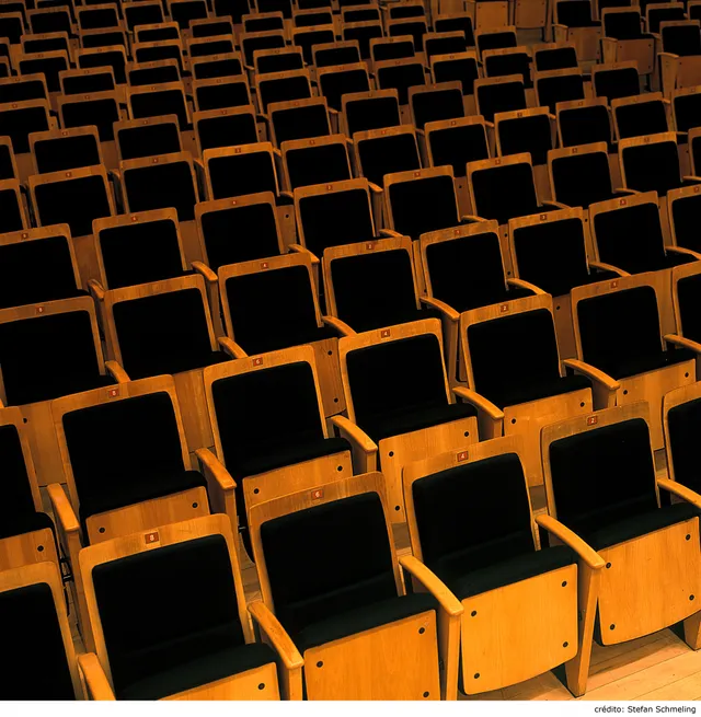 As cadeiras da Sala São Paulo são de madeira amarela e estofado azul. Elas estão vazias e posicionadas lado a lado. 