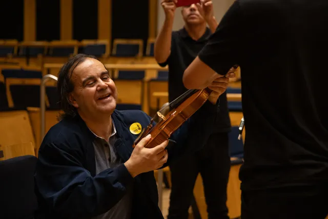 Uma pessoa com deficiência visual toca em um violino apresentada por um educador da Fundação Osesp.